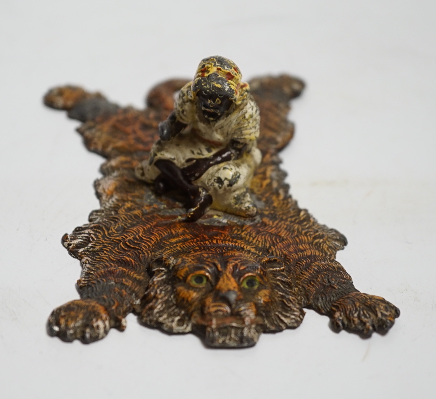 A Bergmann style painted lead figure of a gentleman on a tiger skin, 12.5cm long